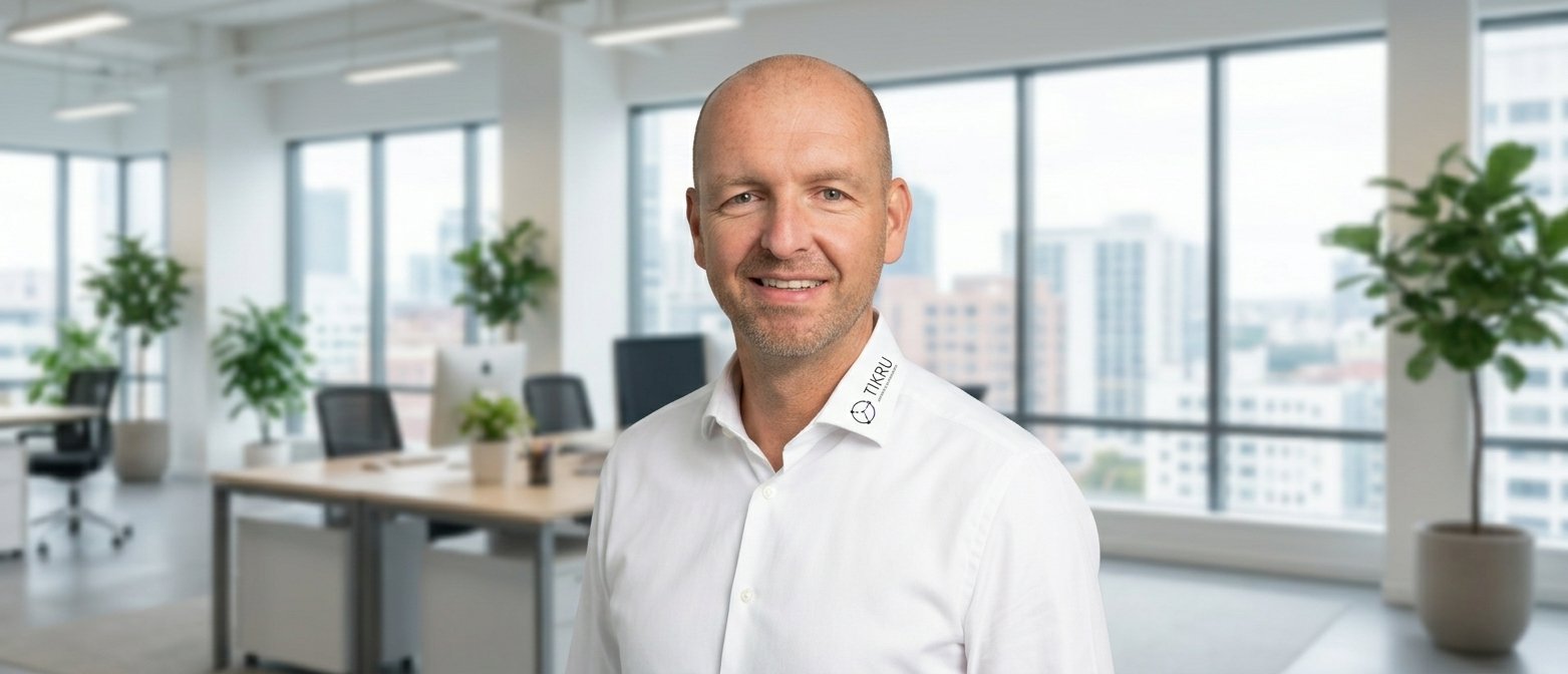Thilo Krumm, Inhaber von TIKRU, lächelt in einem modernen Büro mit Stadtblick. Thilo Krumm, Inhaber von TIKRU, lächelt in einem modernen Büro mit Stadtblick.